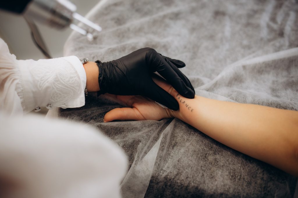 Beautician using laser device to remove an unwanted tattoo from female arm. Concept of erasing t